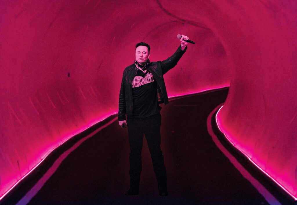 Elon Musk holding up a microphone while standing inside one of his car tunnels. 