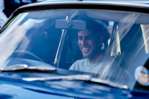 UK Prime Minister Rishi Sunak smiling behind the wheel of a car.