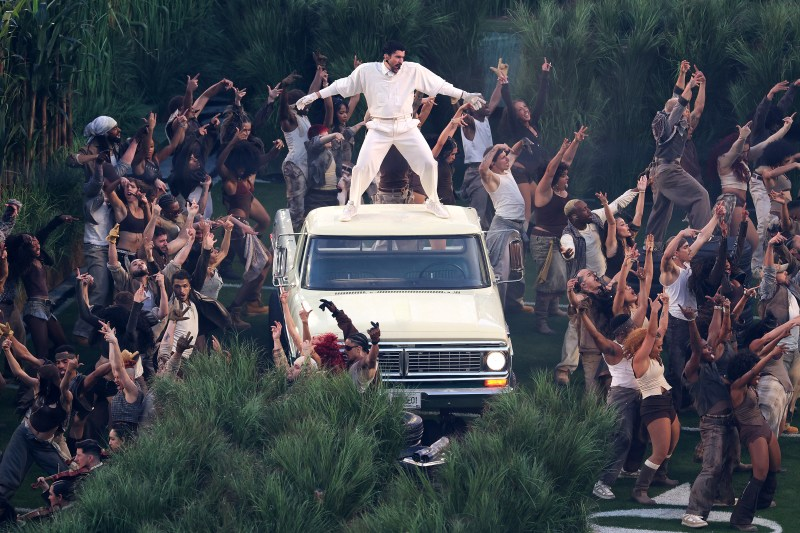 Bad Bunny stands on an old pickup truck wearing a white suit and surrounded by dancers during the Super Bowl show