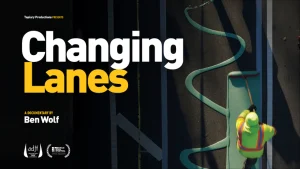 A promotional poster for the documentary film "Changing Lanes," directed by Ben Wolf. The image shows a road worker in high-viz clothing from overhead, painting a traffic lane green.