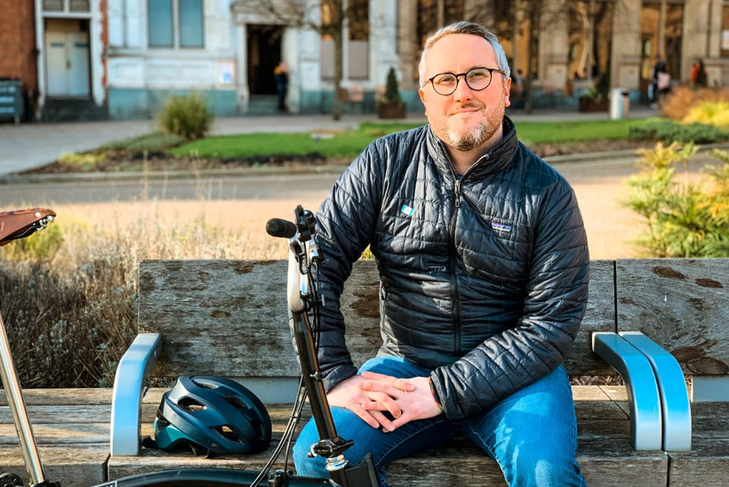 Adam Tranter sits smiling on a bench with his bike helmet next to him