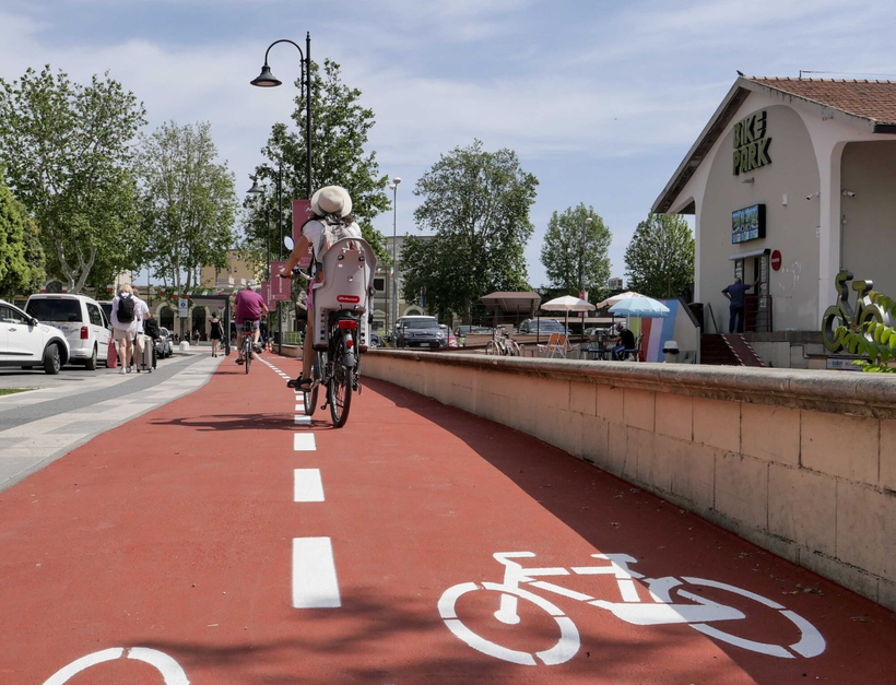 A red-paved protected bike lane in Rimini, Italy, with a rider who has a child on the back of their bike