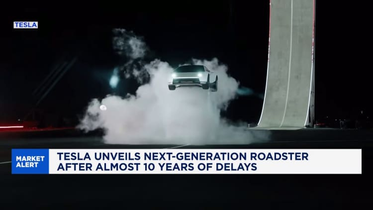 A screenshot of a video of the Tesla next-generation roadster in midair in front of a vertical track, descending in a dramatic cloud of smoke. The chyron says, "Market Alert: Tesla Unveils Next-Generation roadster after almost 10 years of delays."